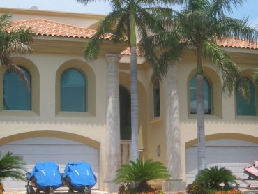A house with palm trees and blue chairs in front of it.